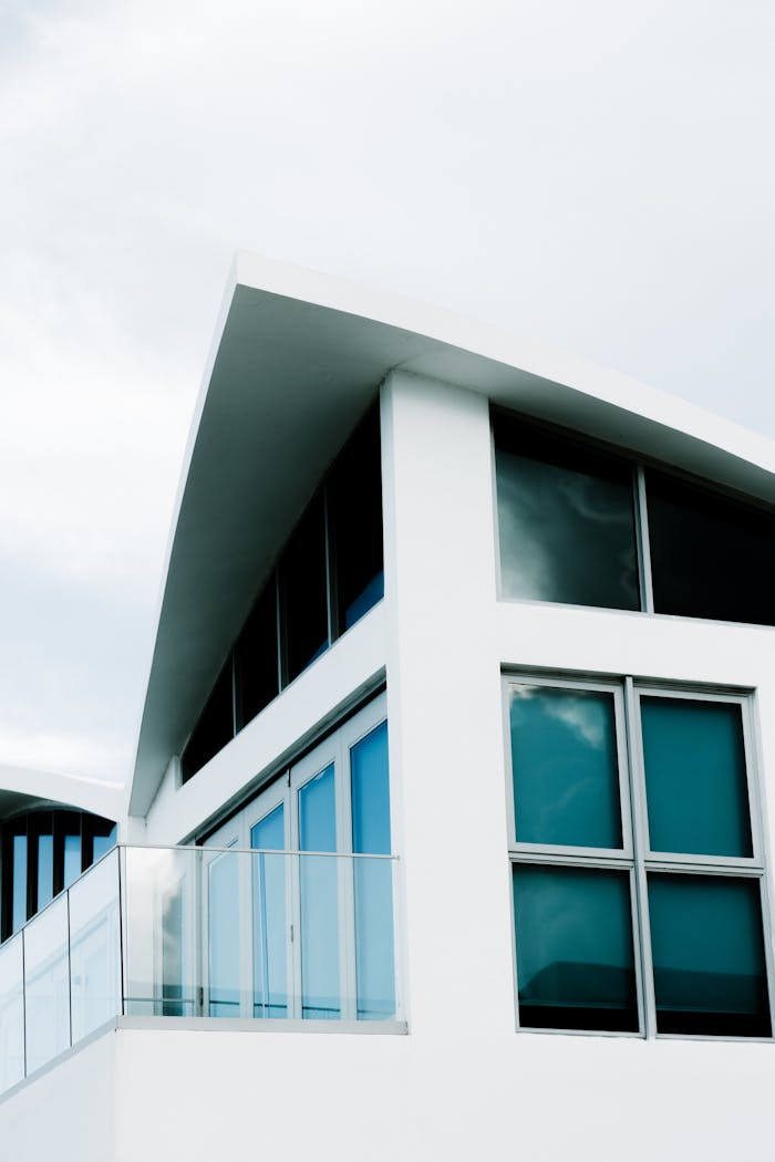 Contemporary white building featuring unique angles and clear glass windows against a soft sky.