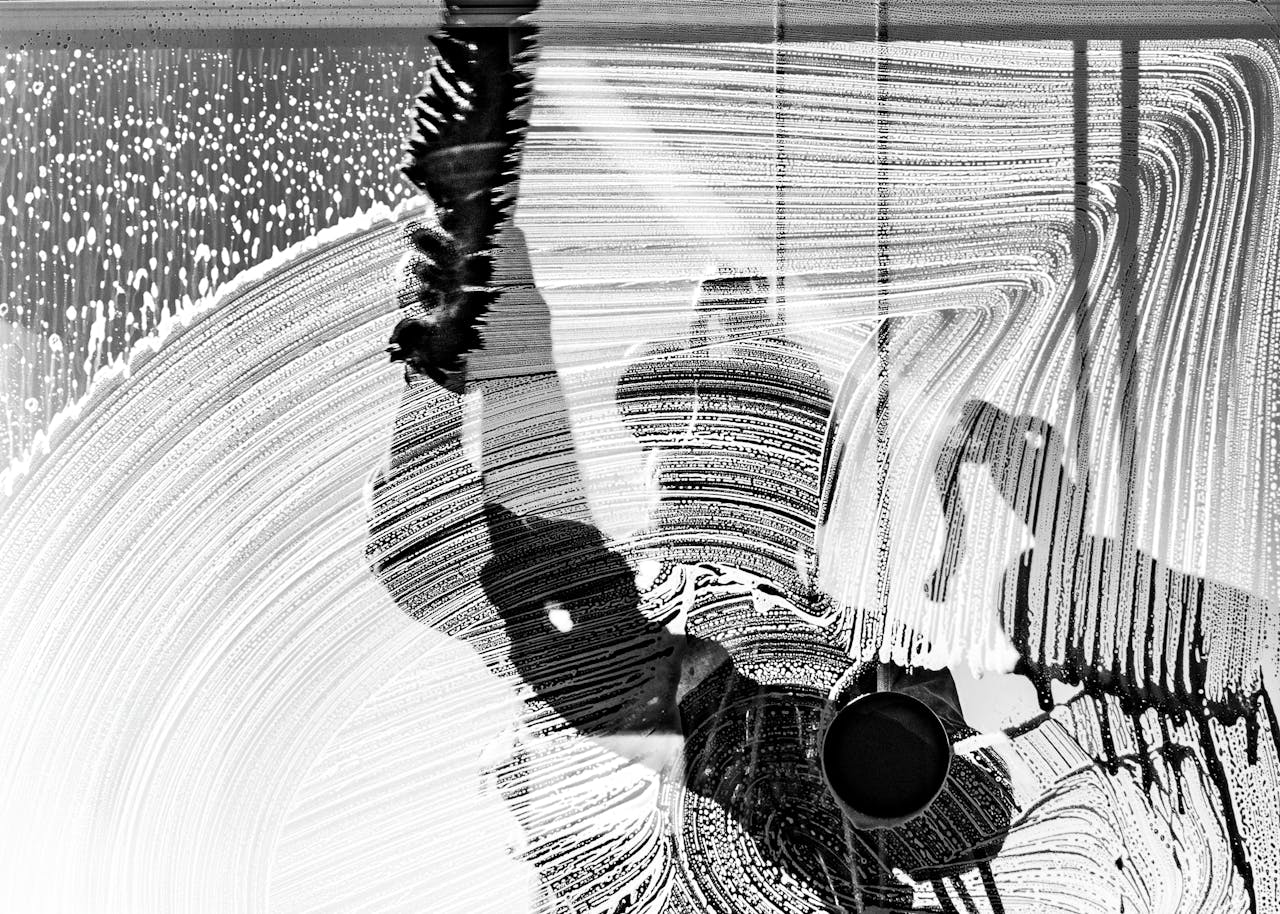 Black and white photo of a window washer at work, captured in Buenos Aires, showcasing urban life and reflections.